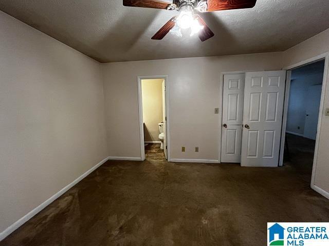 unfurnished bedroom with ceiling fan, ensuite bath, dark carpet, and a textured ceiling