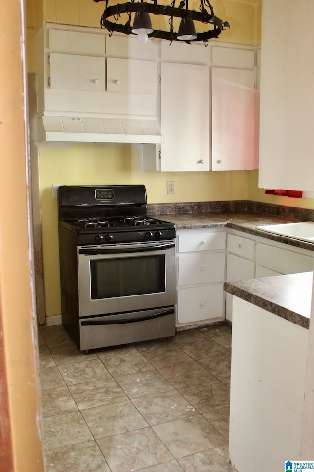 kitchen featuring stainless steel gas range, dark countertops, and white cabinetry