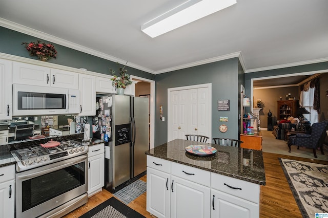 kitchen with crown molding, light hardwood / wood-style flooring, dark stone countertops, appliances with stainless steel finishes, and white cabinets