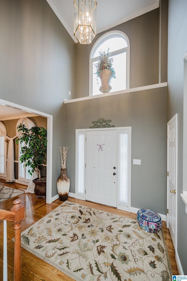 entryway with an inviting chandelier, hardwood / wood-style flooring, ornamental molding, and a high ceiling