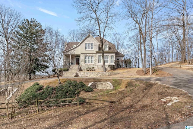 view of front of home featuring aphalt driveway, fence, stone siding, and stucco siding