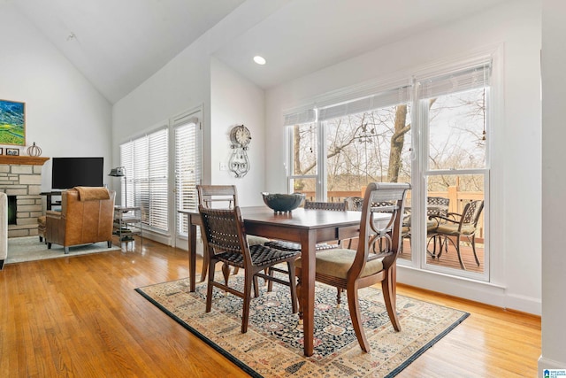 dining area featuring high vaulted ceiling, a fireplace, and light hardwood / wood-style flooring