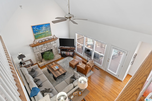 living room with ceiling fan, a stone fireplace, high vaulted ceiling, and light wood-type flooring