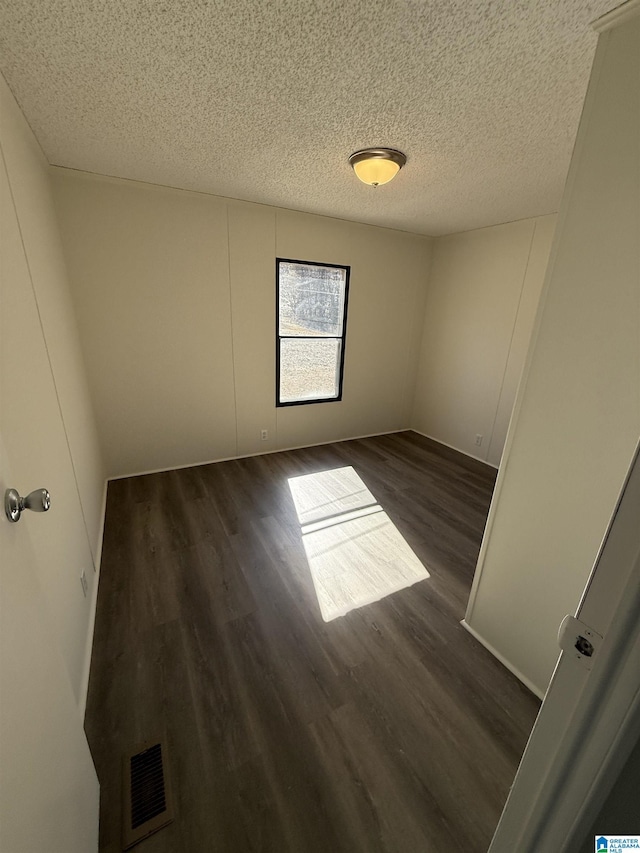 unfurnished room featuring a textured ceiling and dark hardwood / wood-style flooring