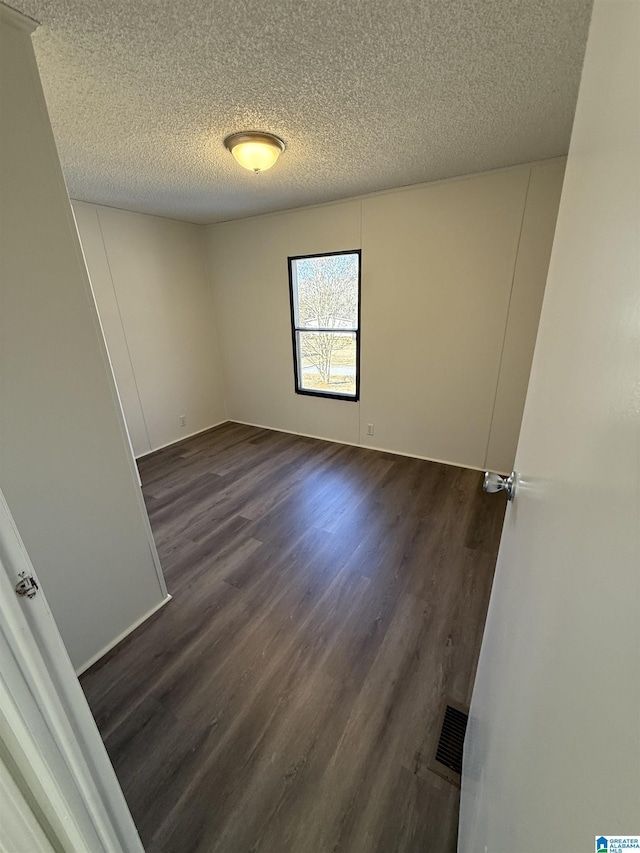 unfurnished room featuring a textured ceiling and dark hardwood / wood-style flooring