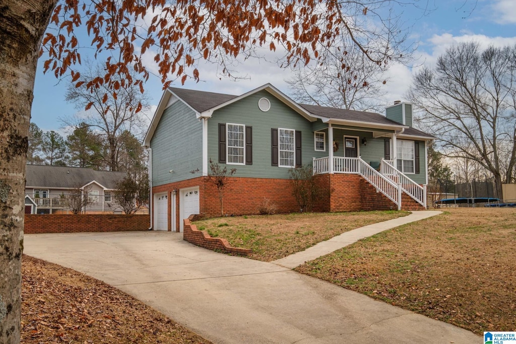 view of front of property featuring a garage, covered porch, a front lawn, and a trampoline