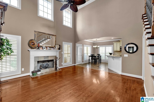 living room featuring hardwood / wood-style flooring, ceiling fan with notable chandelier, ornamental molding, and a tile fireplace