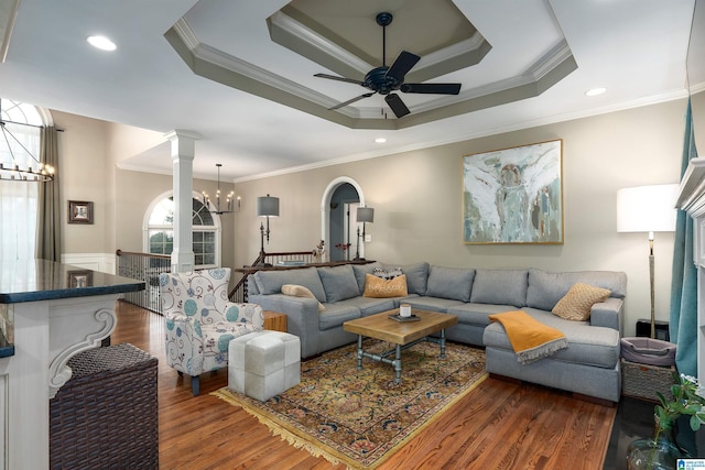 living room featuring ornate columns, ceiling fan with notable chandelier, dark hardwood / wood-style flooring, a tray ceiling, and crown molding