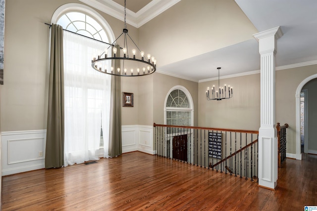 empty room with dark hardwood / wood-style flooring, a notable chandelier, ornamental molding, and ornate columns