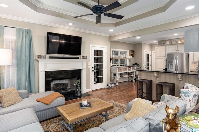 living room featuring dark hardwood / wood-style floors, ornamental molding, a raised ceiling, and ceiling fan