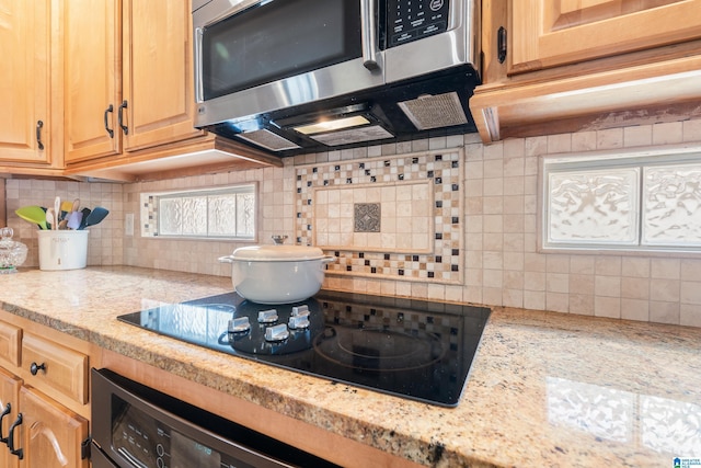 kitchen with light brown cabinets, black electric stovetop, light stone counters, and decorative backsplash