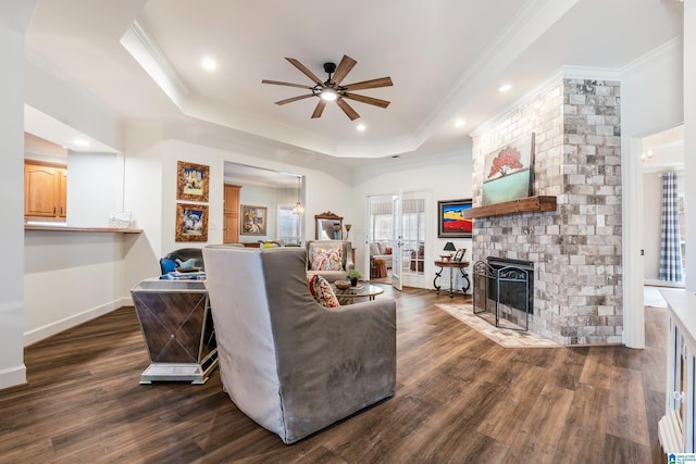 living room featuring ornamental molding, a brick fireplace, dark wood-type flooring, and a tray ceiling