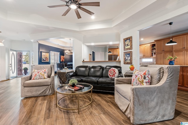 living room featuring hardwood / wood-style flooring, a raised ceiling, ornamental molding, and ceiling fan with notable chandelier