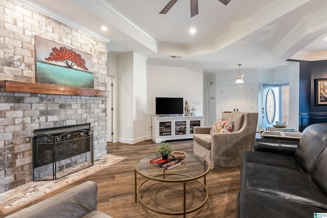 living room with crown molding, ceiling fan, a fireplace, dark hardwood / wood-style flooring, and a raised ceiling