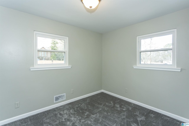 unfurnished room featuring dark colored carpet, visible vents, and baseboards