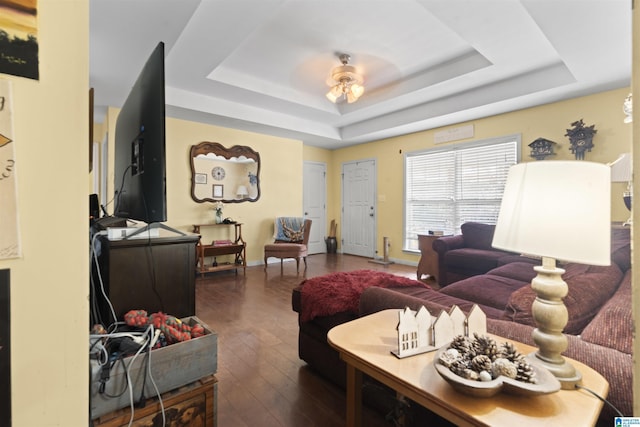 living room with a tray ceiling, dark hardwood / wood-style floors, and ceiling fan