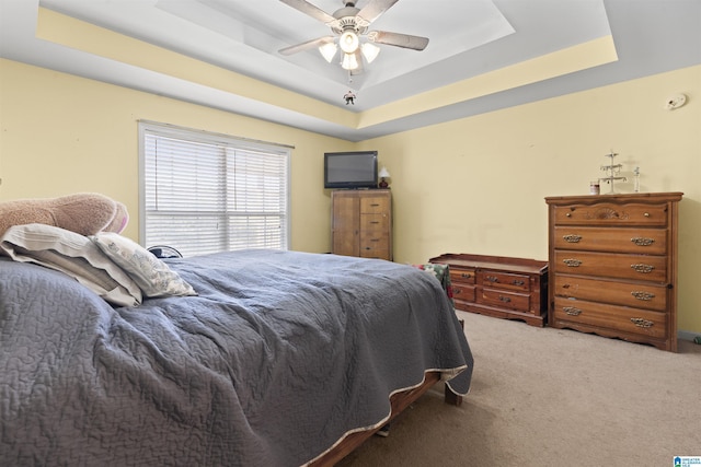 carpeted bedroom with a raised ceiling and ceiling fan