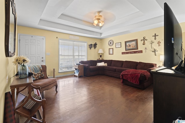 living room with dark wood-type flooring, ceiling fan, and a raised ceiling