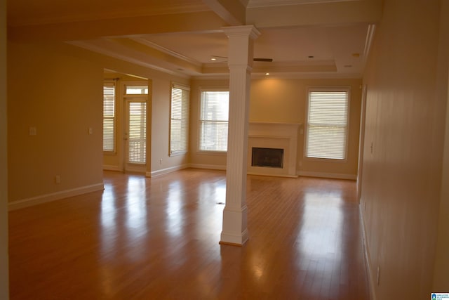 unfurnished living room with ornamental molding, a raised ceiling, decorative columns, and light wood-type flooring