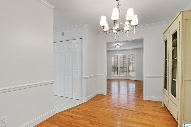 unfurnished dining area with an inviting chandelier, ornamental molding, a textured ceiling, and light wood-type flooring