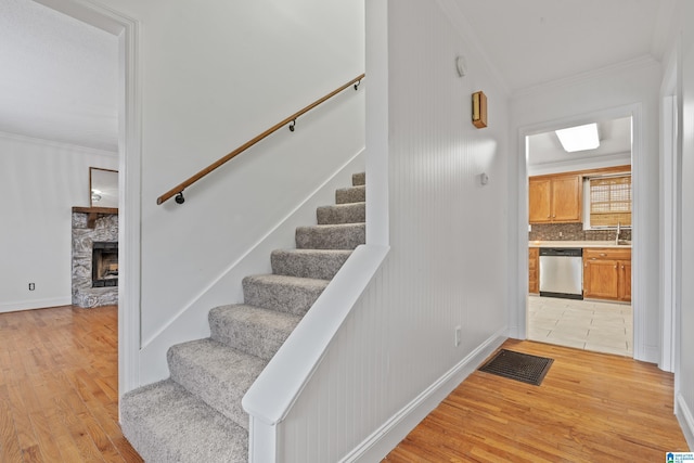 stairs featuring ornamental molding, a stone fireplace, sink, and wood-type flooring