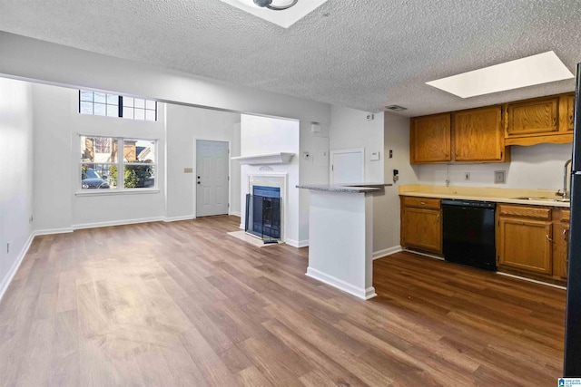 kitchen featuring a skylight, black dishwasher, wood-type flooring, a textured ceiling, and kitchen peninsula