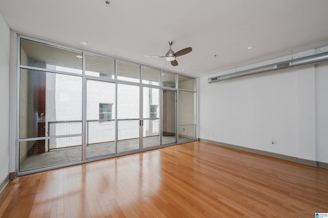 spare room featuring wood-type flooring, ceiling fan, and a wall of windows