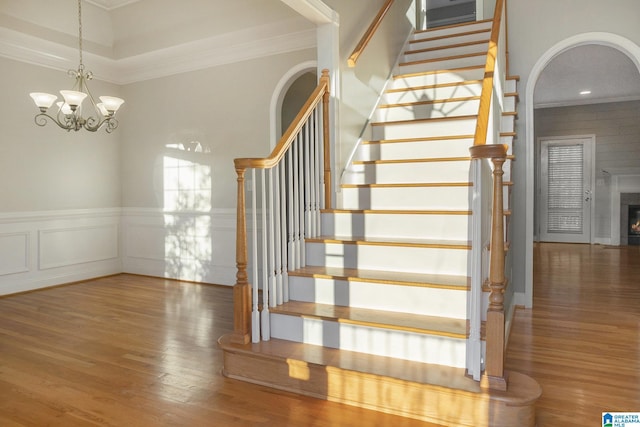 stairway with an inviting chandelier, crown molding, and wood-type flooring