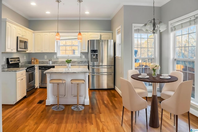 kitchen featuring a kitchen island, appliances with stainless steel finishes, pendant lighting, white cabinetry, and light stone counters