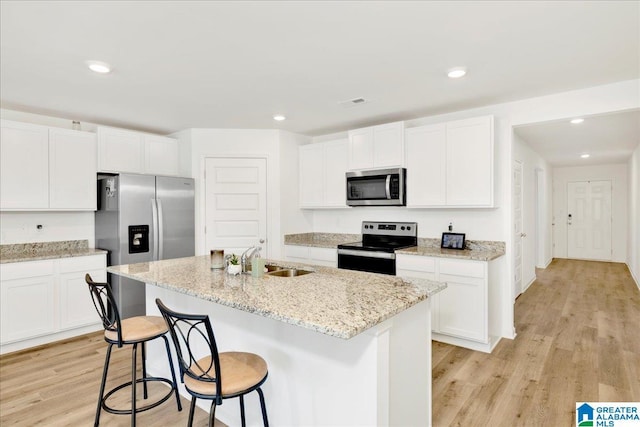 kitchen featuring white cabinetry, a center island with sink, light wood-type flooring, appliances with stainless steel finishes, and light stone countertops