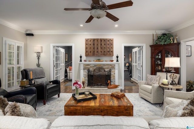 living room featuring crown molding, a stone fireplace, ceiling fan, and light wood-type flooring