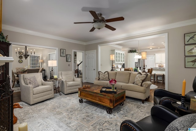 living room with crown molding, ceiling fan with notable chandelier, a fireplace, and light wood-type flooring