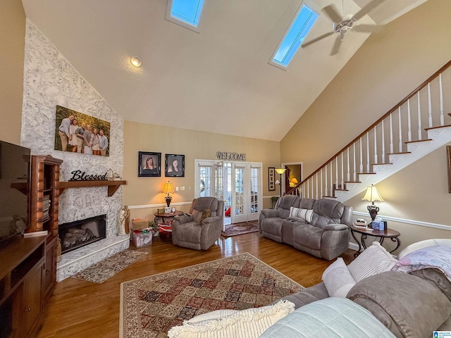 living room with hardwood / wood-style flooring, ceiling fan, a skylight, high vaulted ceiling, and a stone fireplace