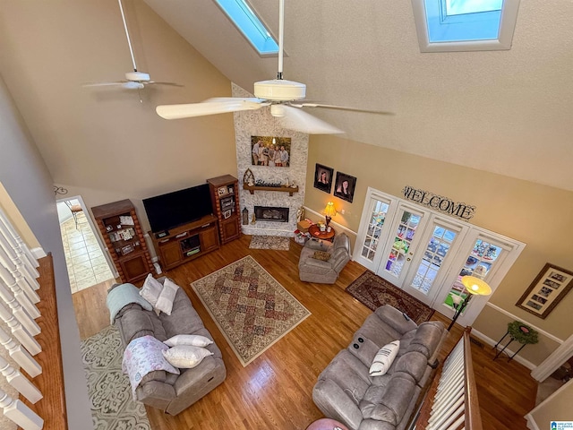 living room with a skylight, high vaulted ceiling, hardwood / wood-style flooring, ceiling fan, and a fireplace