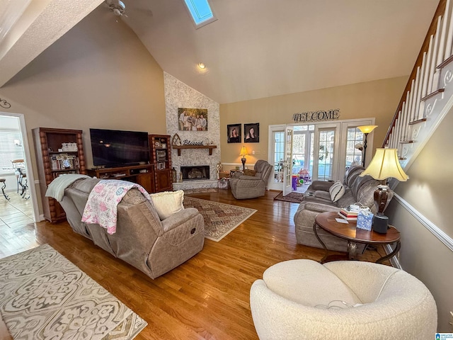 living room with a stone fireplace, hardwood / wood-style floors, high vaulted ceiling, and a skylight