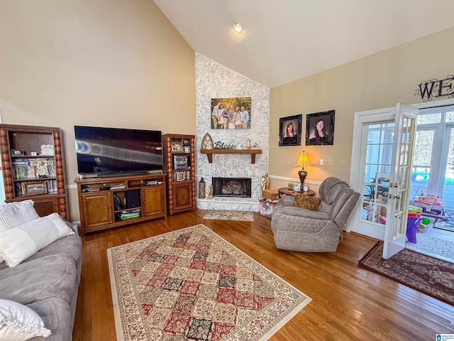 living room with hardwood / wood-style floors, a stone fireplace, high vaulted ceiling, and french doors