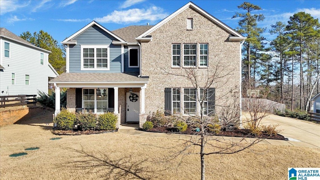 traditional-style home featuring driveway, roof with shingles, fence, and brick siding
