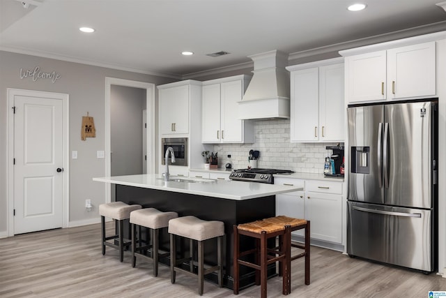 kitchen featuring stainless steel refrigerator with ice dispenser, white cabinetry, custom range hood, and a center island with sink