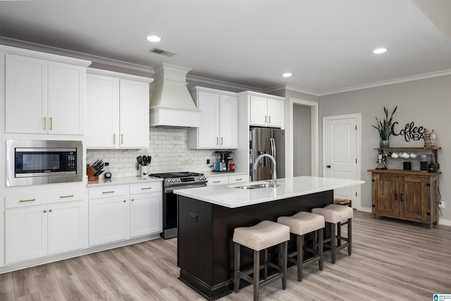 kitchen with white cabinetry, appliances with stainless steel finishes, custom range hood, and a center island with sink