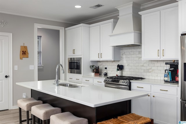 kitchen with premium range hood, a breakfast bar, sink, white cabinetry, and an island with sink