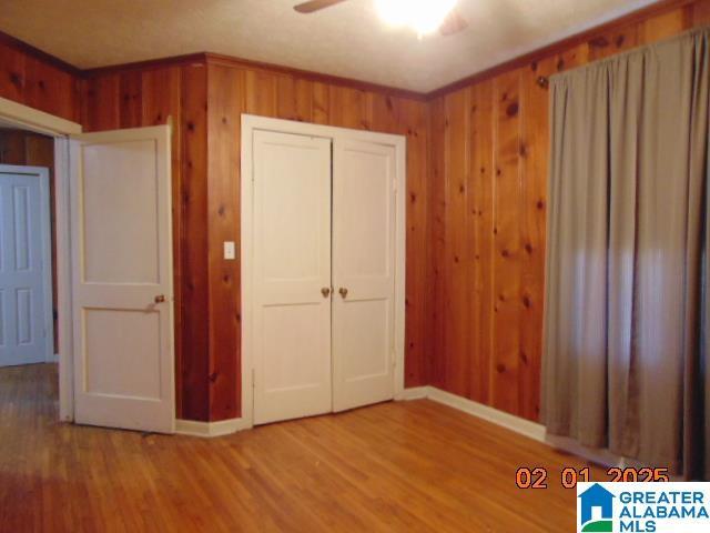 unfurnished bedroom with crown molding, ceiling fan, wooden walls, and hardwood / wood-style floors