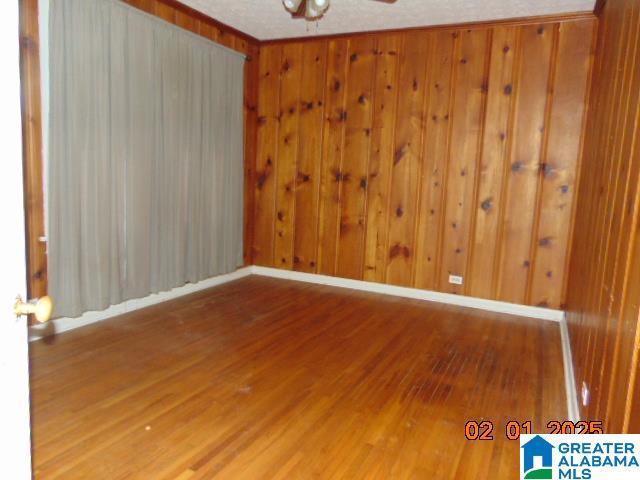 unfurnished room featuring ceiling fan, wooden walls, and hardwood / wood-style floors