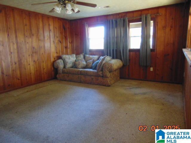 unfurnished living room with wood walls, ceiling fan, and carpet flooring