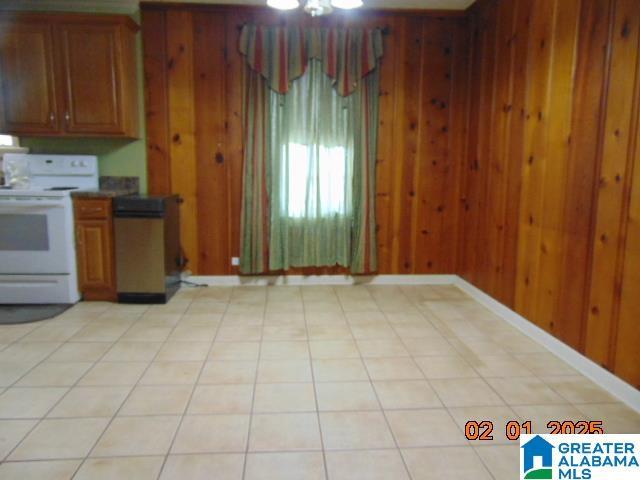 kitchen featuring electric stove, light tile patterned flooring, and wood walls