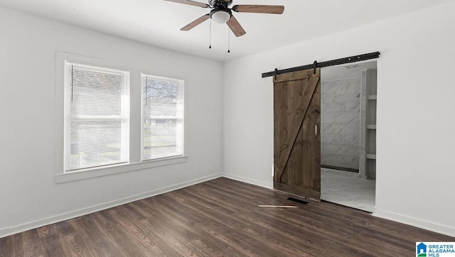 unfurnished room featuring dark hardwood / wood-style floors, ceiling fan, and a barn door