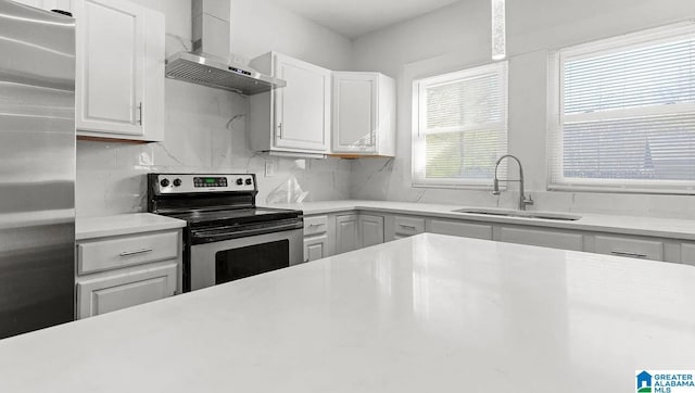 kitchen featuring white cabinetry, sink, backsplash, stainless steel appliances, and wall chimney range hood