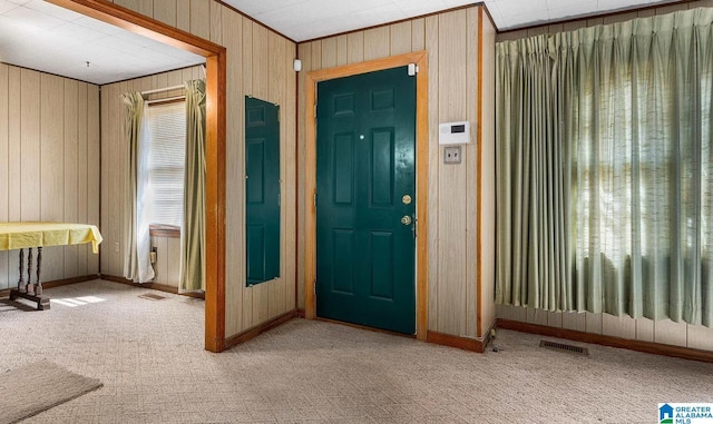 carpeted foyer featuring ornamental molding and wood walls