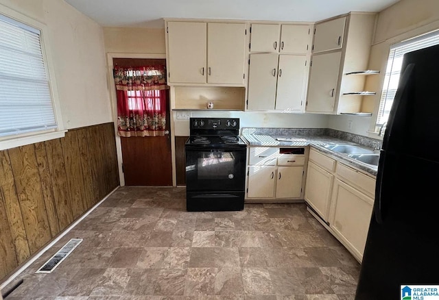 kitchen with cream cabinetry, sink, wood walls, and black appliances