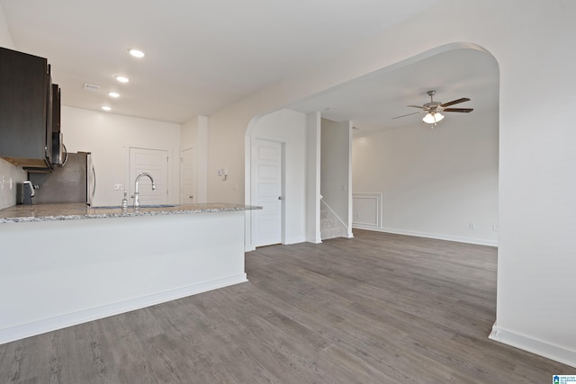 kitchen with sink, ceiling fan, light stone counters, dark hardwood / wood-style flooring, and kitchen peninsula