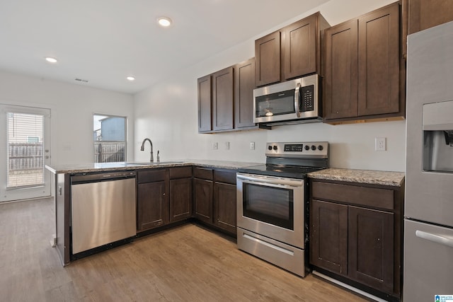 kitchen featuring sink, light hardwood / wood-style flooring, appliances with stainless steel finishes, light stone countertops, and kitchen peninsula